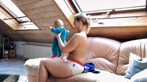 Curvy topless blonde with huge tits holding baby on couch in white panties