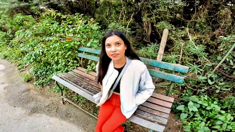 Sexy brunette Indian teen with long hair smiling on park bench in red pants