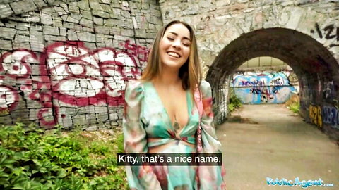 Smiling brunette babe in deep cleavage revealing colorful dress under graffiti archway in outdoor public agent tease