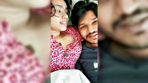 Indian couple selfie in hotel bed, sexy girlfriend in pink low-cut top showing cleavage with boyfriend
