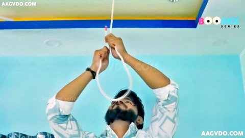 Bearded South Asian man in shirt gripping white rope from ceiling in blue-walled room